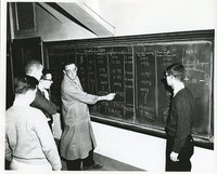 Faculty member instructing students at chalkboard