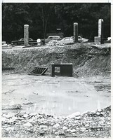 Carney Hall exterior under construction with puddle, debris, and view of cars on street