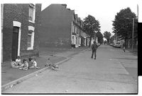 Children playing, unconcerned by British Army foot patrol on the street, Springfield Road, Belfast