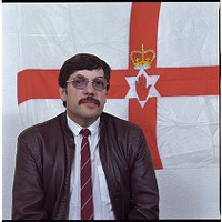 Andy Tyrie in front of Ulster flag, Ulster Defense Association Headquarters, Gawn St., Newtownards Road, Belfast
